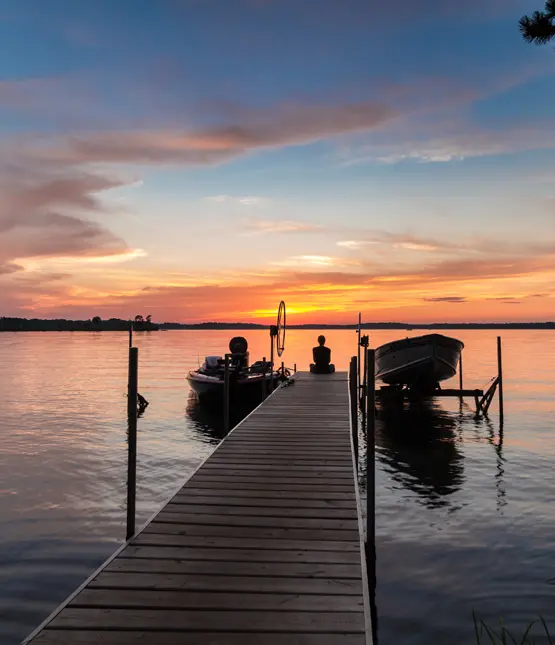 Wooden dock extending into a lake with boats moored alongside at sunset